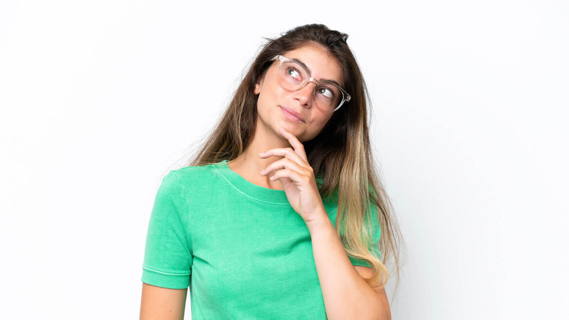 Whatsapp Marketing - Na imagem tem uma mulher branca, sobre um fundo branco, usando uma camisa verde, óculos e posando fazendo expressão de pensativa.