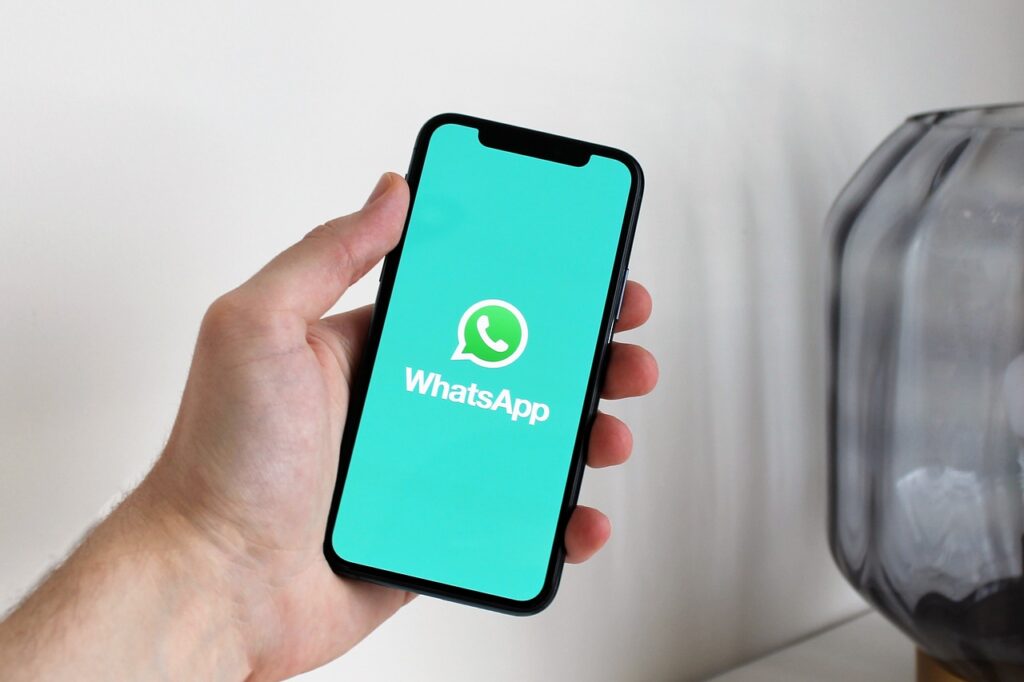 WhatsApp Marketing para aumentar o lucro - a imagem que ilustra o tópico tem o fundo de uma sala onde aparece uma mão, segurando um celular com a logo do WhatsApp aberta na tela em destaque.