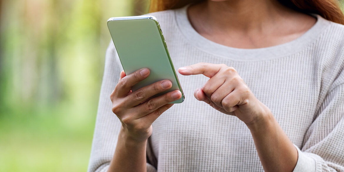 mensagens automáticas - imagem de uma mulher, ao ar livre, vestindo uma blusa branca, segurando um celular e apontando para a tela.