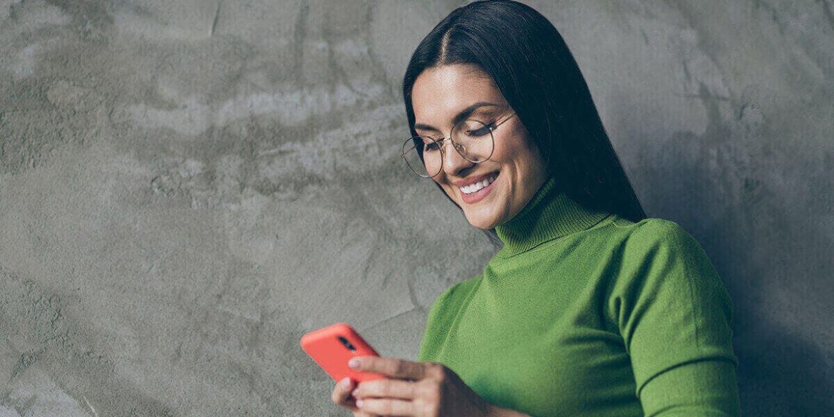 Marketing no WhatsApp - Imagem de uma mulher com uma blusa verde e de óculos de grau, mexendo no celular.