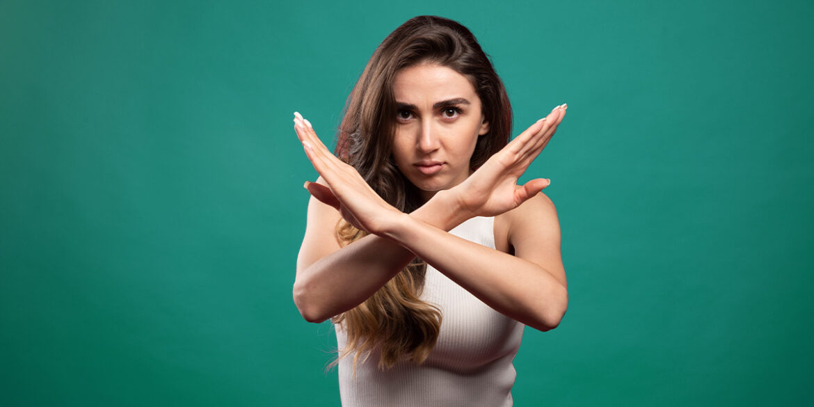 Banimento no WhatsApp - A imagem que ilustra o tema tem o fundo verde escuro e, no meio, em destaque, tem uma mulher branca, de cabelo longo castanho, usando uma blusa regata branca com os braços cruzados formando um 