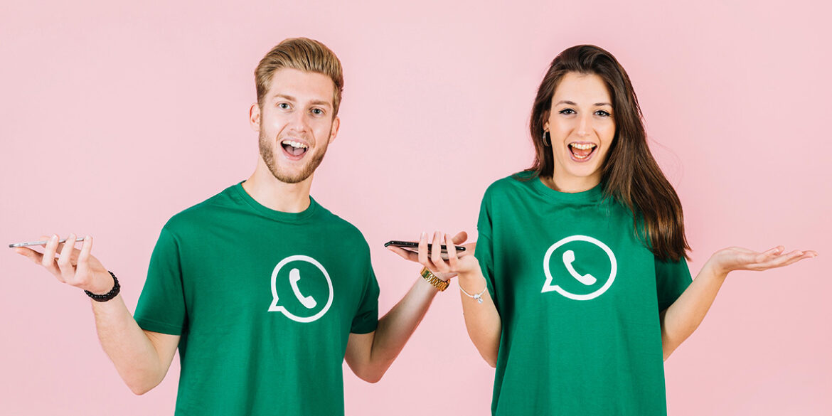 WhatsApp Business ou Site - A imagem que ilustra o tema tem o fundo rosa com duas pessoas sobre ele usando uma camisa verde com o logotipo do WhatsApp. Uma das pessoas é um homem branco, de cabelo e barba ruivos, um relógio dourado e com ambas as mãos levantadas na altura do ombro, segurando um celular em uma das mãos, fazendo expressão de indecisão. A outra pessoa é uma mulher, branca, de cabelo liso escuro, com as mãos também levantadas na altura dos ombros, em uma das mãos está segurando um celular e fazendo expressão de indecisão.