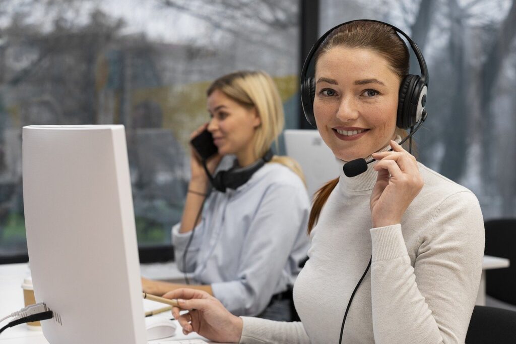 organização de respostas para os clientes - IMAGEM DE DUAS MULHERES REALIZANDO ATENDIMENTO EM FRENTE A COMPUTADORES.