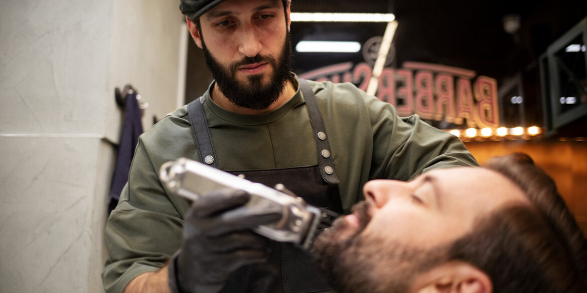 Etiquetas fundamentais para barbearias - A imagem que ilustra o tema tem uma barbearia de fundo e, em destaque, um barbeiro fazendo a barba de um cliente.