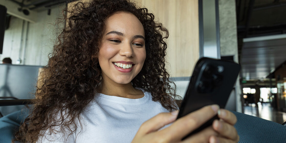 Catálogo do WhatsApp temático - a imagem que ilustra o tema tem o fundo de uma sala, onde aparece uma mulher sentada, mexendo no celular e sorrindo.