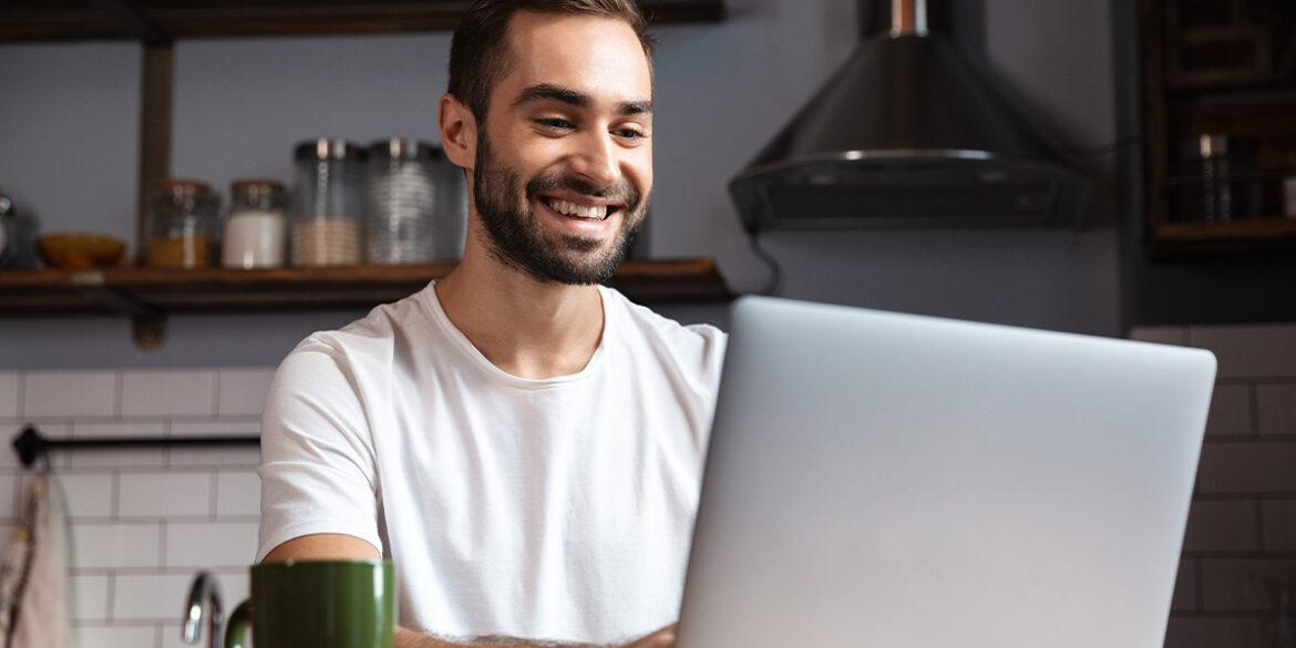 sem celular - a imagem que ilustra o tema tem o fundo de uma sala e, em destaque, tem um homem sentado em frente uma mesa onde tem um computador sobreposto para o qual o homem está olhando e sorrindo.