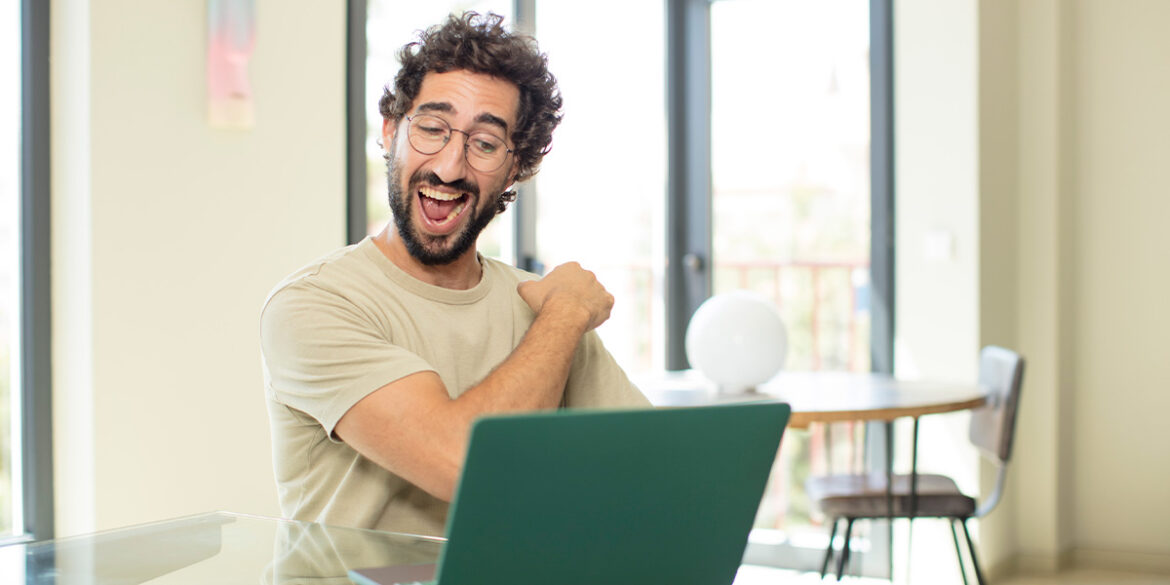 Taxa de abertura no WhatsApp - a imagem que ilustra o tema tem o fundo de uma sala e, em destaque, aparece um homem sentado em frente uma mesa onde tem um computador sobreposto e, o homem, tá fazendo expressão de feliz.