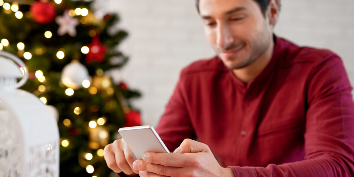 Catálogo WhatsApp Business para o Natal - A imagem que ilustra o tema tem um homem sentado mexendo no celular e de fundo uma sala com decoração natalina.