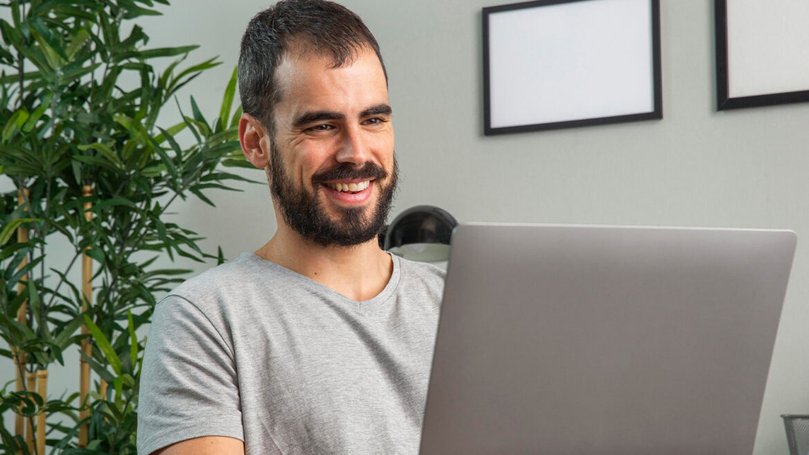 WhatsApp Business para profissionais liberais - A imagem que ilustra o tema tem o fundo de uma sala, onde aparece um homem sentado em frente a um computador olhando para a tela e sorrindo.