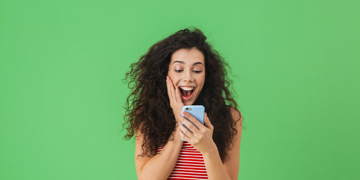 Principais novidades WhatsApp em 2024 - A imagem que ilustra o tema tem o fundo verde e no meio uma mulher segurando um celular, olhando para ele e fazendo uma expressão feliz de surpresa.