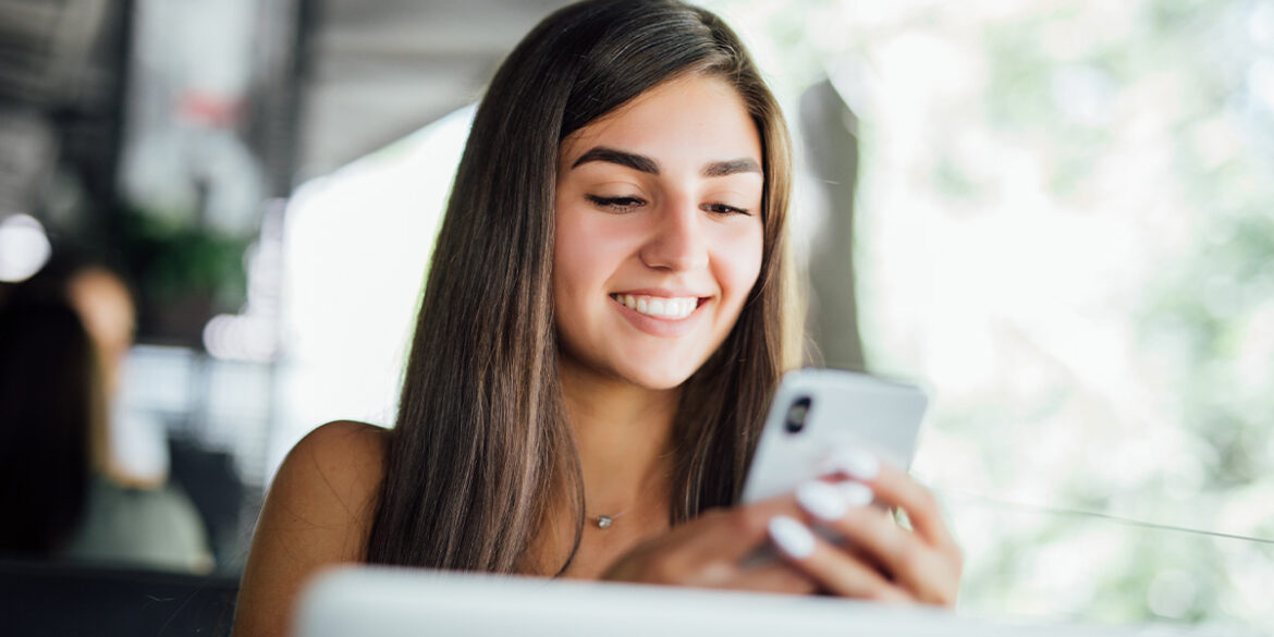 Menina sorrindo e mexendo no celular, em busca de leads qualificados