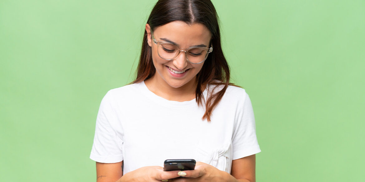 Menina mexendo no celular e sorrindo, porssivelmente por que recebeu mensagens personalizadas no WhatsApp