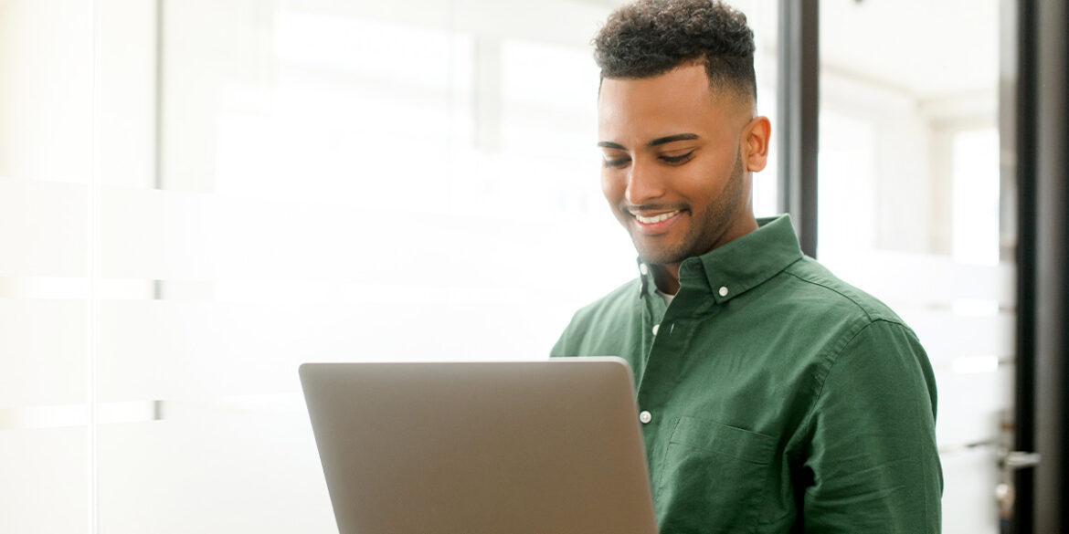 Homem num escritório, mexendo no notebook e recebendo um atendimento híbrido.