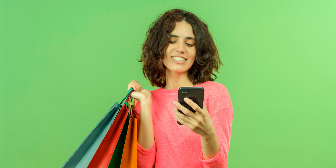 Mulher com sacolas em uma mão, o celular na outra e olhando o WhatsApp Shop