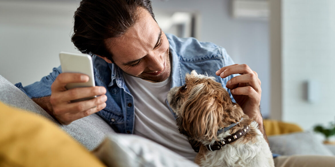Homem sentado no sofa com seu cachorro e mexendo no celular falando com o pet shop
