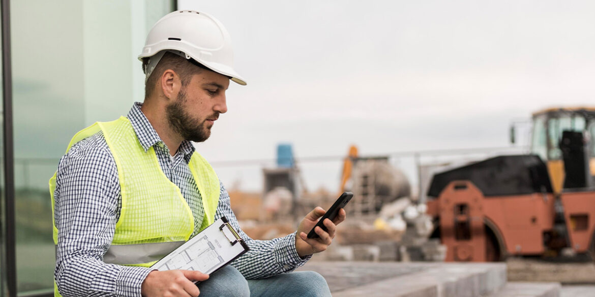 Engenheiro numa construção, mexendo no celular.