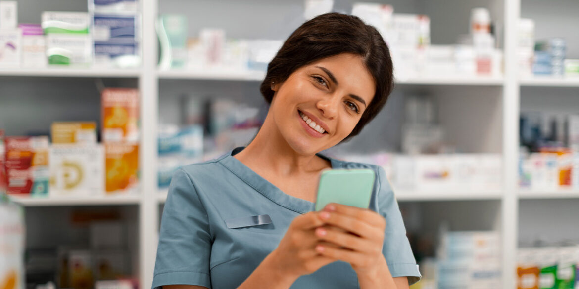 Uma farmacêutica, numa farmácia, com o celular na mão.