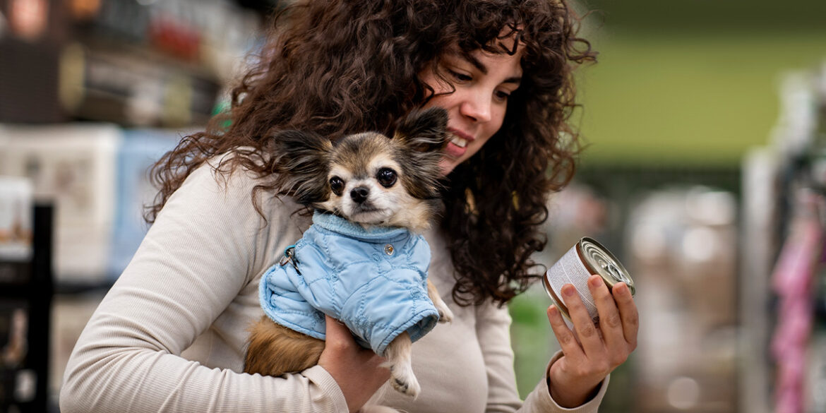 Mulher com um cachorrinho no colo e um petisco na mão.