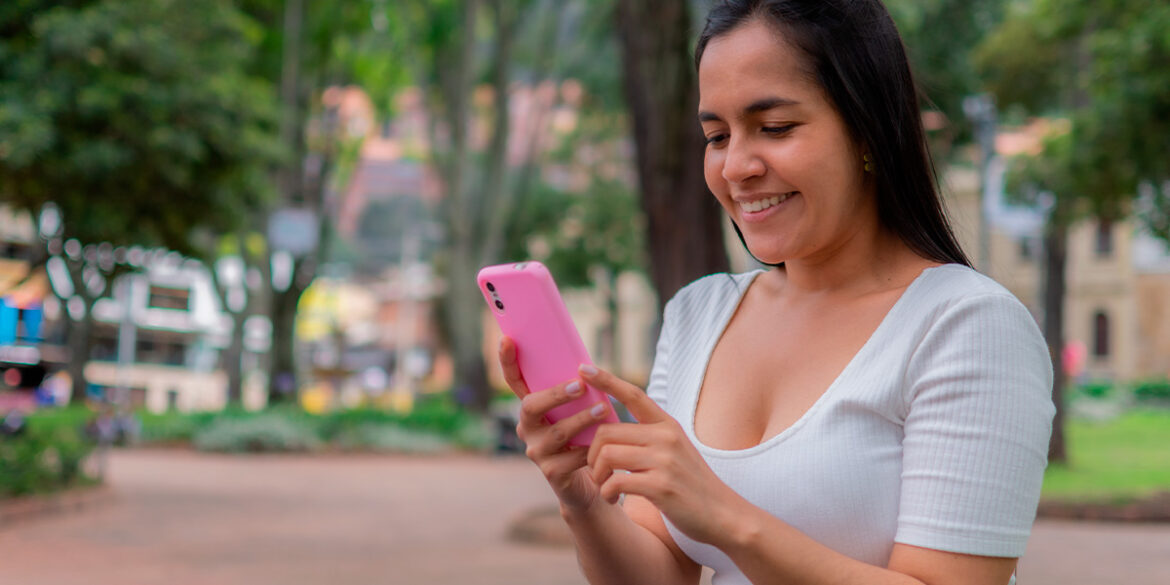 Mulher numa praça mexendo no celular.