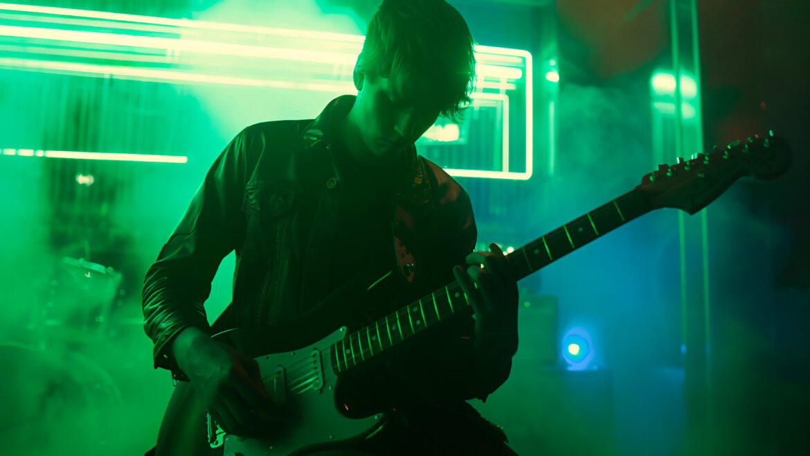 Homem se apresentando e tocando guitarra.