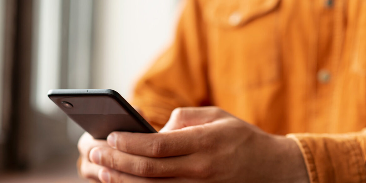 Pessoa com uma camisa laranja e o celular na mão, recebendo um atendimento no whatsapp