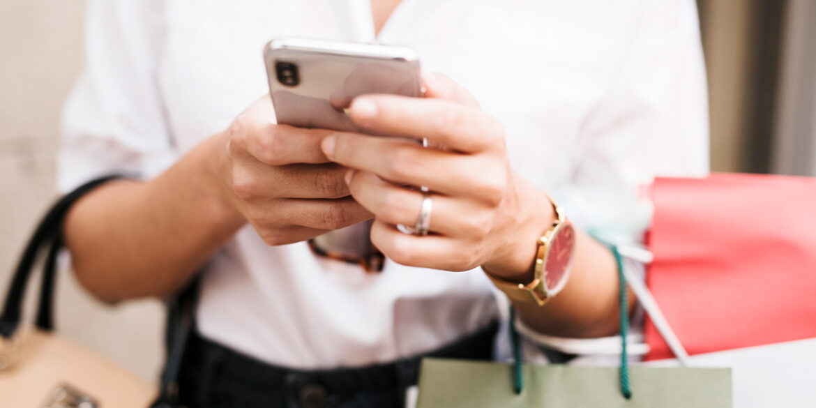 Mulher com o celular na mão e várias salcolar de compras.